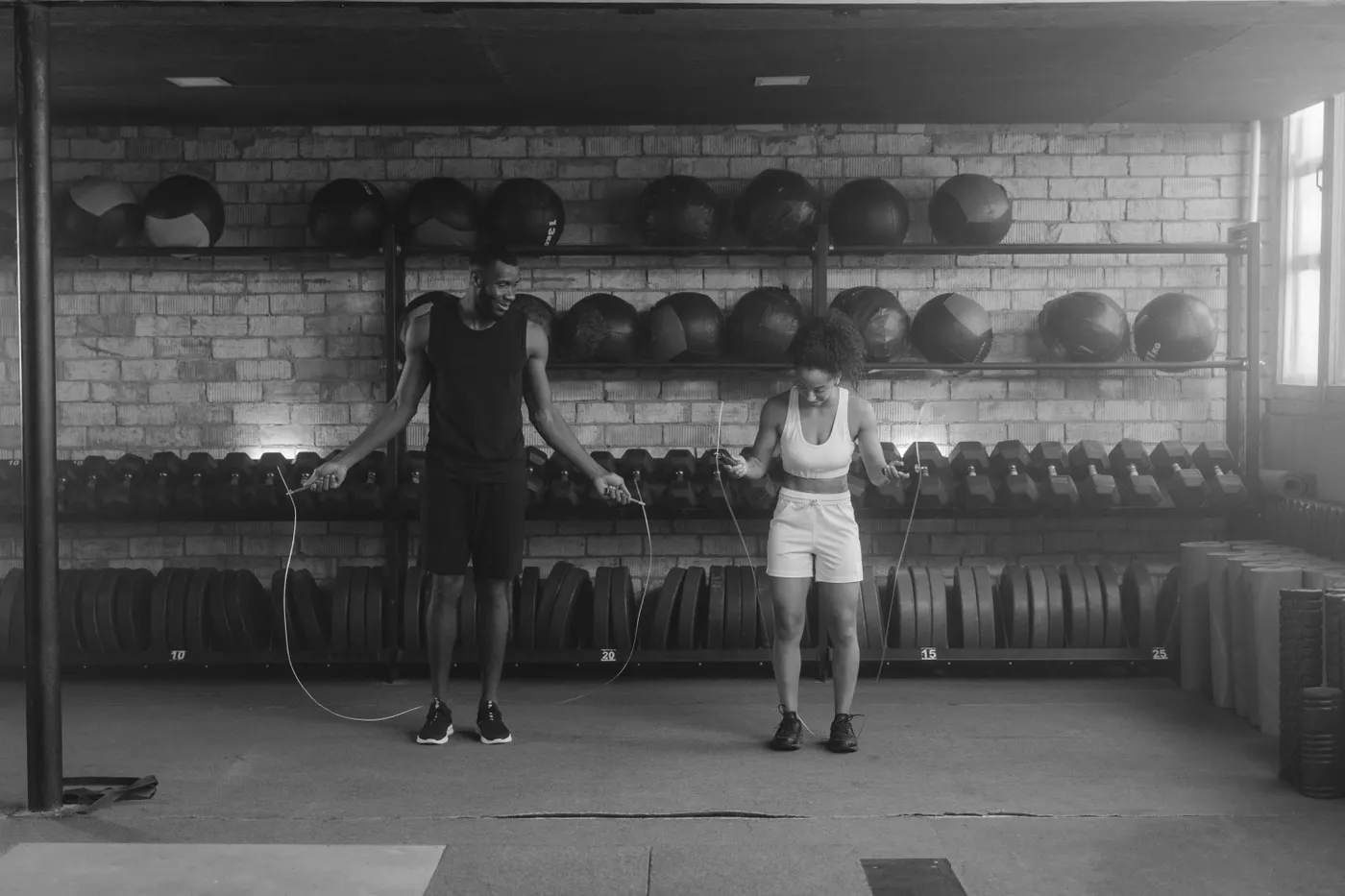 Two people practising rope skipping side by side in a gym