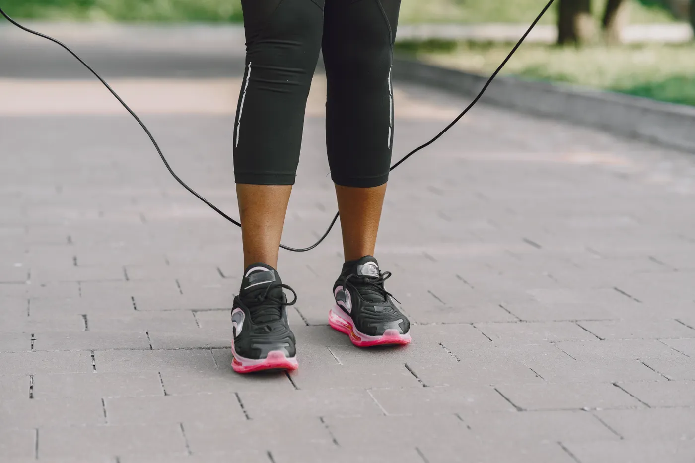 Close-up of sneakers mid-jump over a skipping rope on pavement