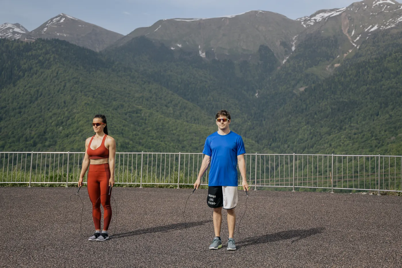 Two adults skipping rope on an outdoor deck with mountains behind
